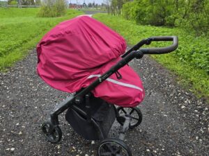 Teel seisab lapsevanker, millel o roosa vihmakile. On suvi, puud ja rohi on taustal rohelised.