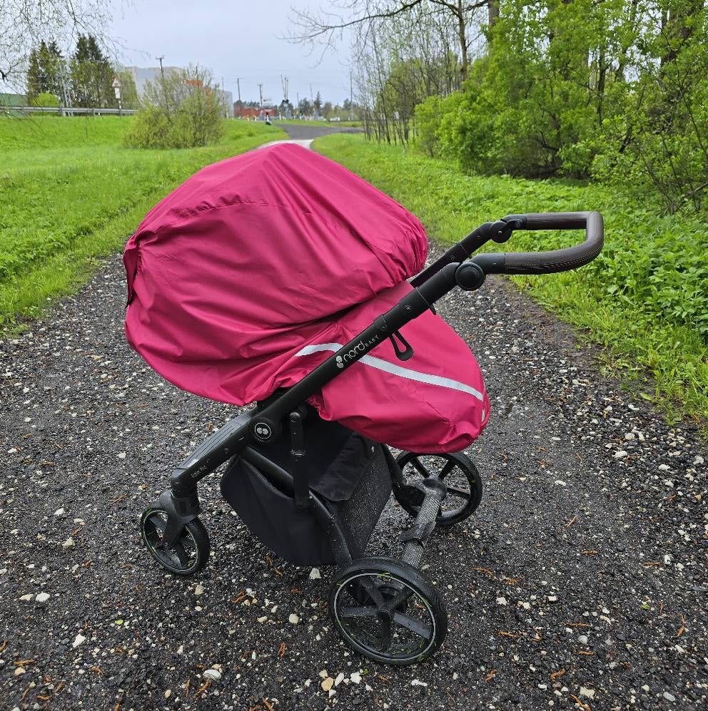 Teel seisab lapsevanker, millel o roosa vihmakile. On suvi, puud ja rohi on taustal rohelised.